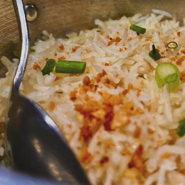 Close-up of Filipino garlic fried rice (sinangag) with green onions and crispy garlic bits, with a spoon.