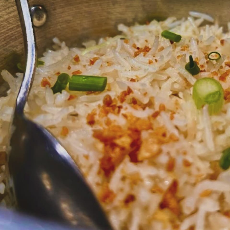 Close-up of Filipino garlic fried rice (sinangag) with green onions and crispy garlic bits, with a spoon.