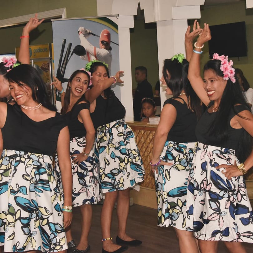 Filipino women in black tops and floral skirts dancing joyfully at Nipa Hut Bar & Restaurant.