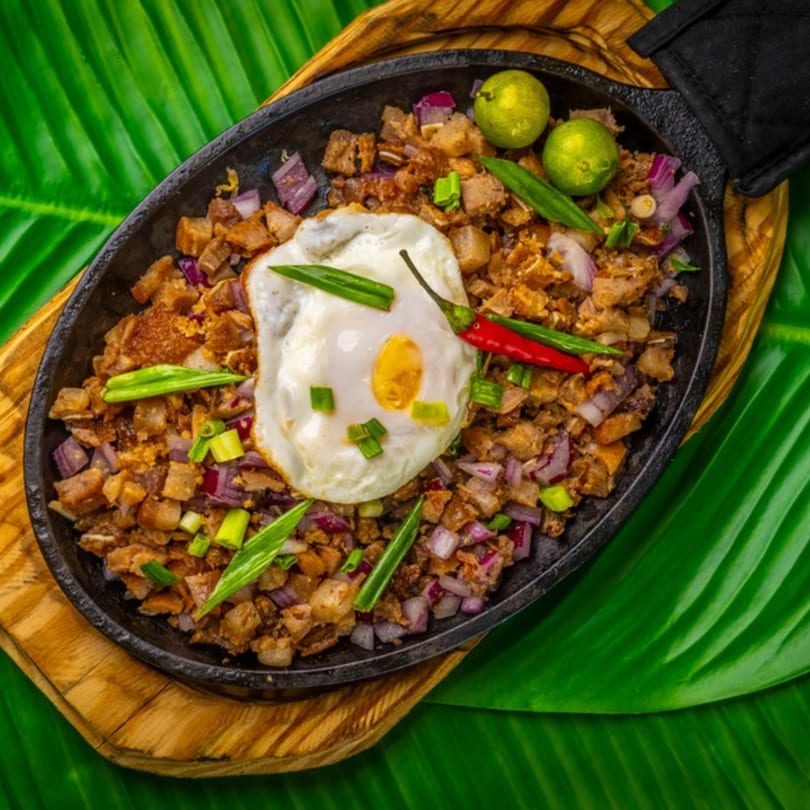 Filipino sisig with a fried egg, red onions, chilies, and calamansi on a sizzling plate.