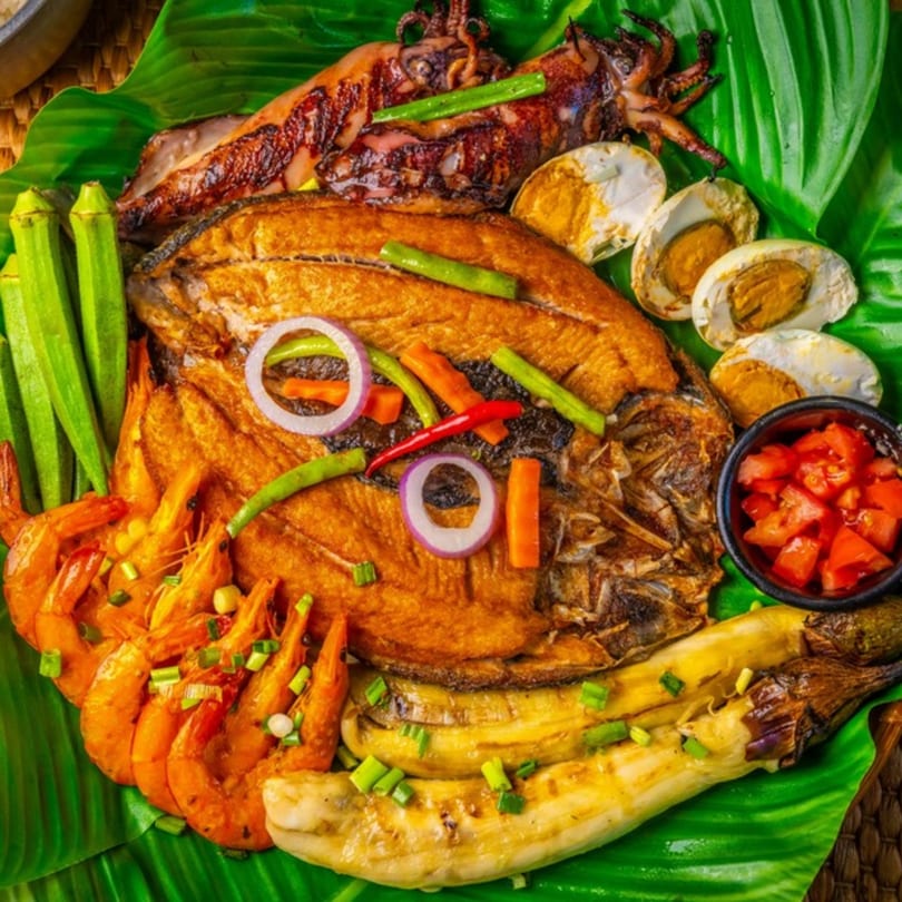 Filipino grilled seafood platter with fish, squid, shrimp, vegetables, and salted eggs on banana leaves.