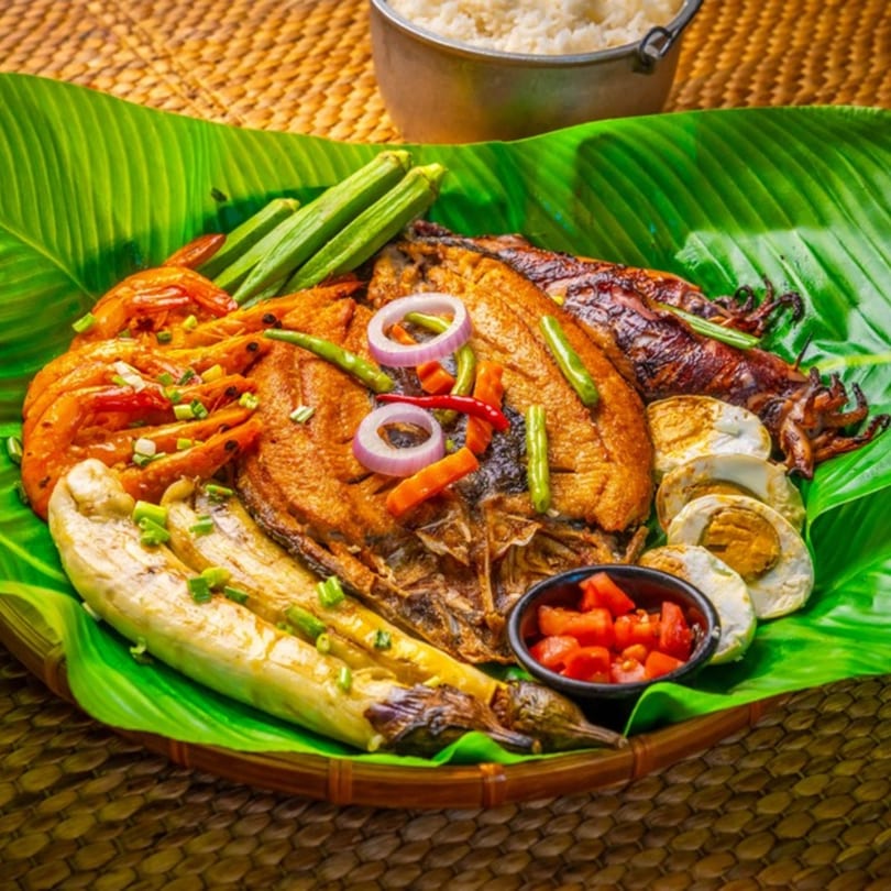 A Filipino boodle fight platter with grilled fish, shrimp, squid, eggplant, okra, and salted eggs.