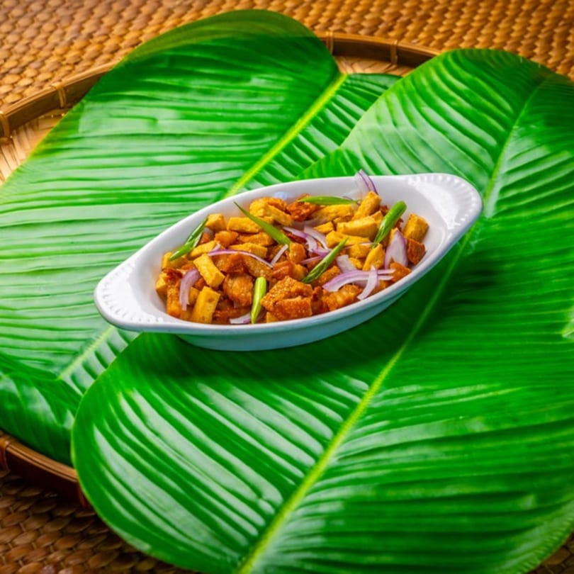 Filipino tofu and pork belly dish, Tokwa't Baboy, in a white bowl on banana leaves.