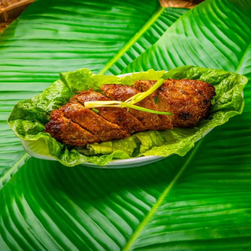 Filipino grilled pork belly (Inihaw na Liempo) slices on lettuce, garnished with green onions.