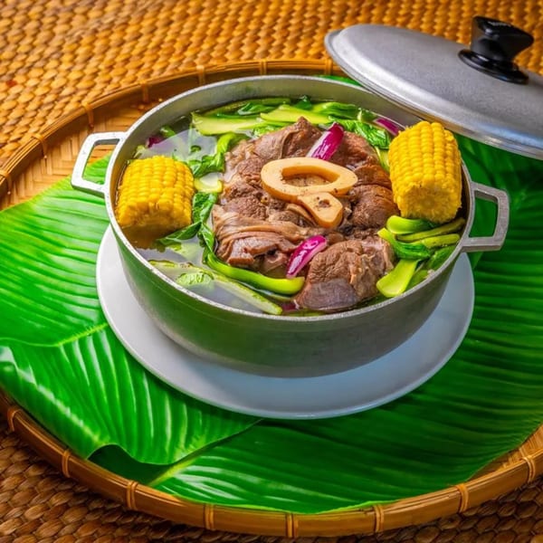A large pot of Filipino Bulalo soup with beef, corn, and vegetables on a banana leaf.