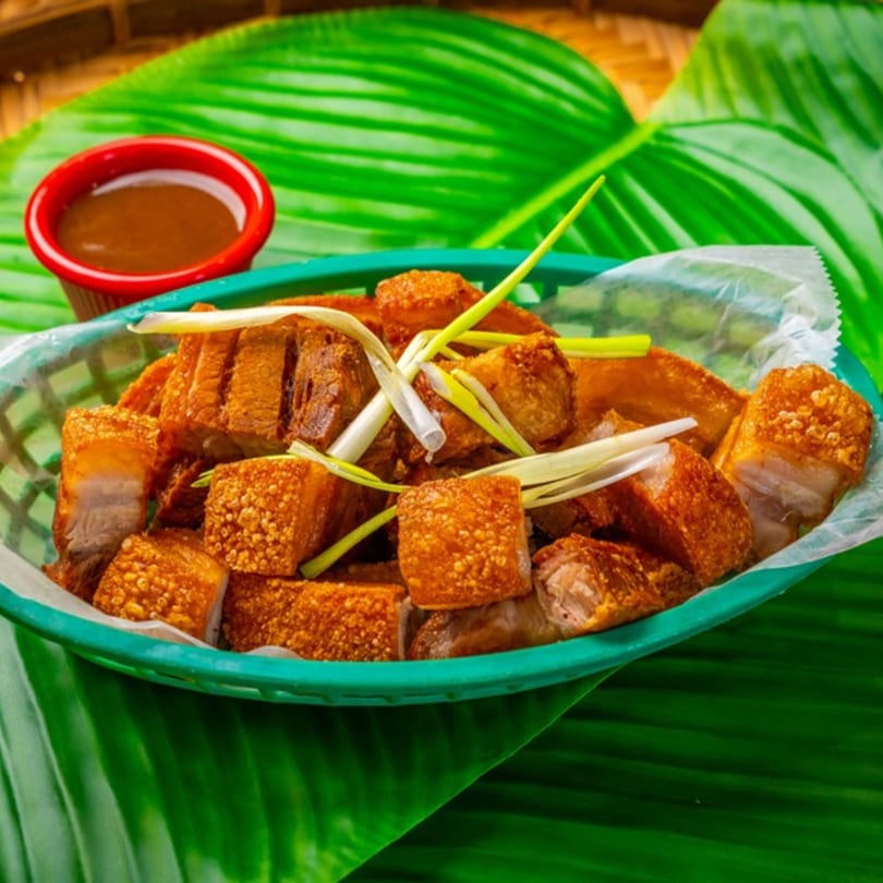 Crispy Filipino Lechon Kawali, deep-fried pork belly pieces, garnished with scallions, served with dipping sauce.