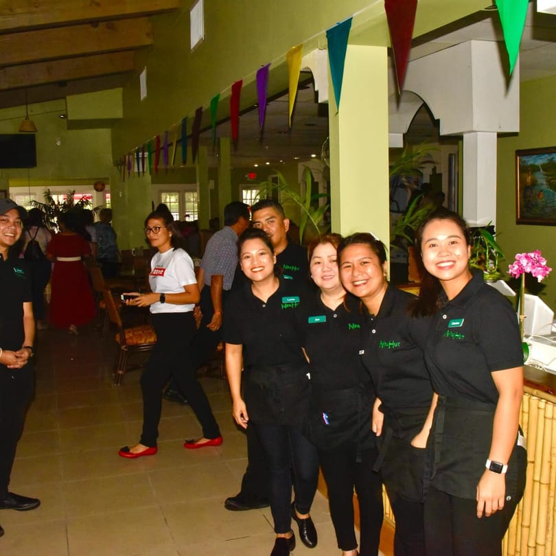 Smiling Nipa Hut staff in black uniforms with aprons, standing in the restaurant dining area.